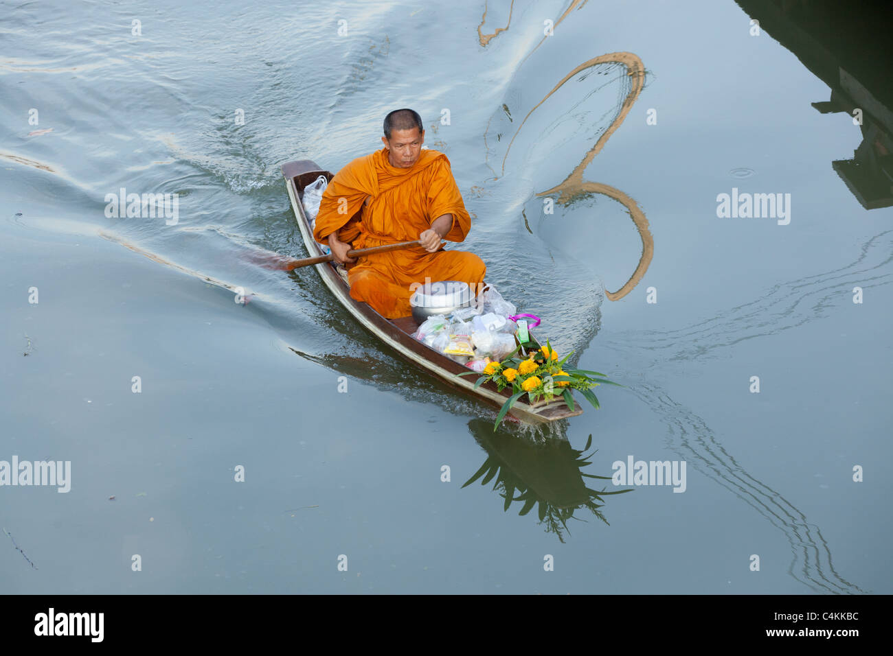 Thai buddhist monk rowing boat early in the morning at amphawa floating market, thailand to take morning offering food. Stock Photo