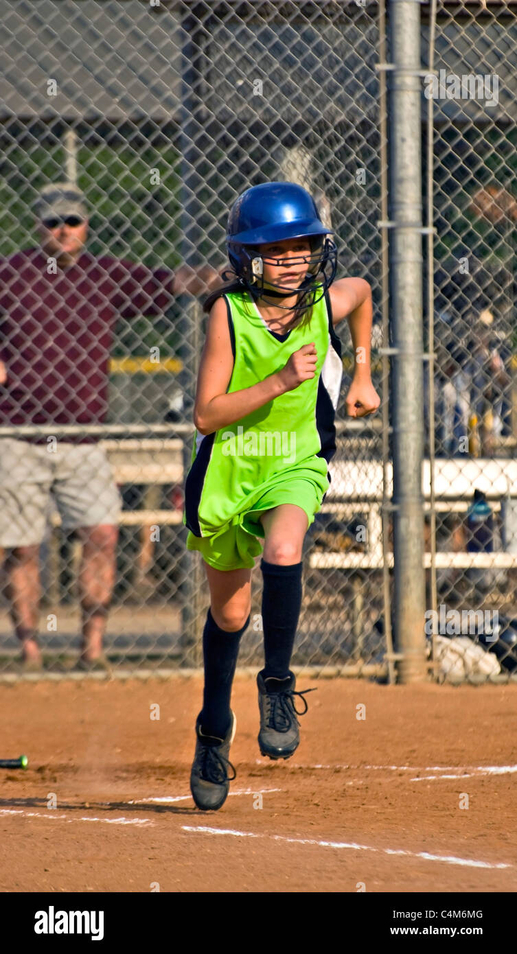A preteen girl running to first base after making a hit, her coach