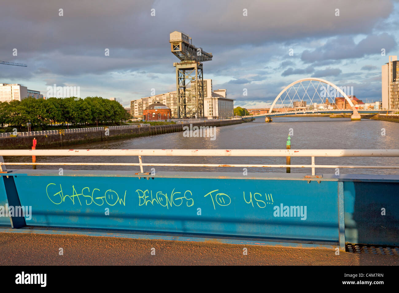 'Glasgow Belongs to Us' graffiti on Bell's Bridge over the River Clyde, looking towards the Finnieston Crane and the Glasgow Arc Stock Photo