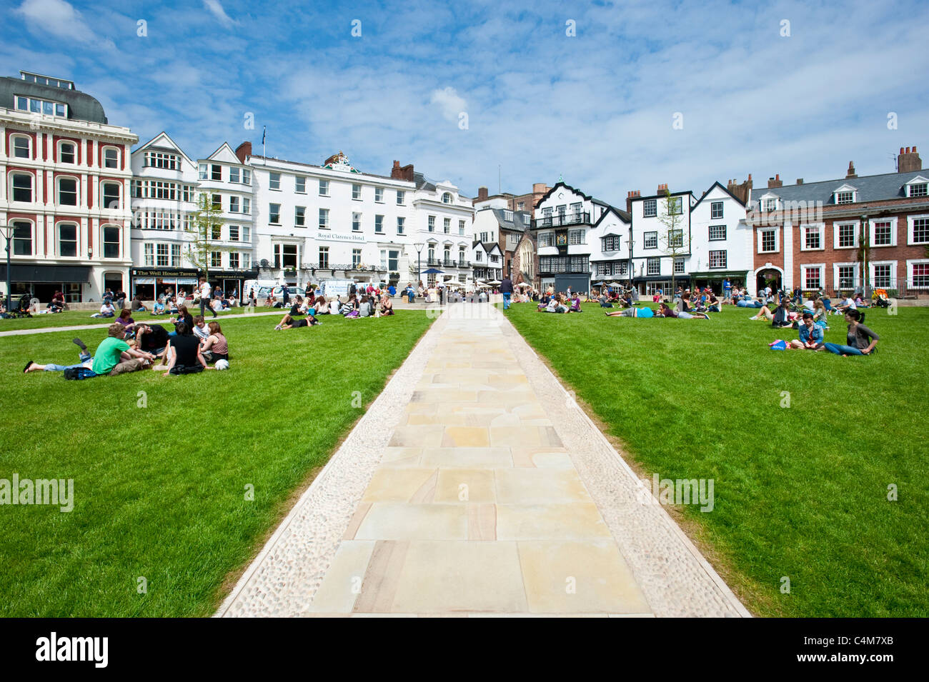 The green of Exeter Cathedral where there are many cafes, bars and restaurants with people relaxing in the sun on the grass. Stock Photo