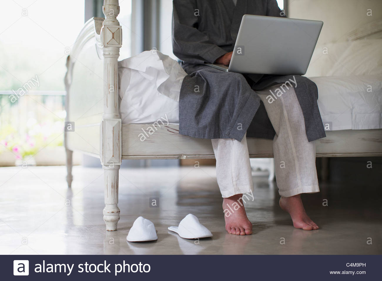 Senior Man With Bare Feet Sitting On Edge Of Bed Using