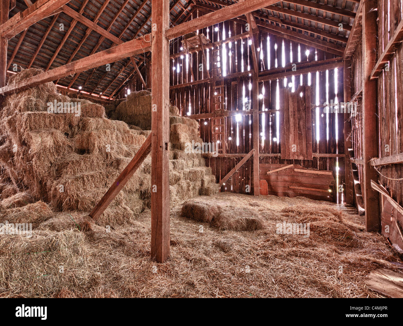 Old Barn with the sun streaming from outside and straw and hay on the floor of the hayloft Stock Photo