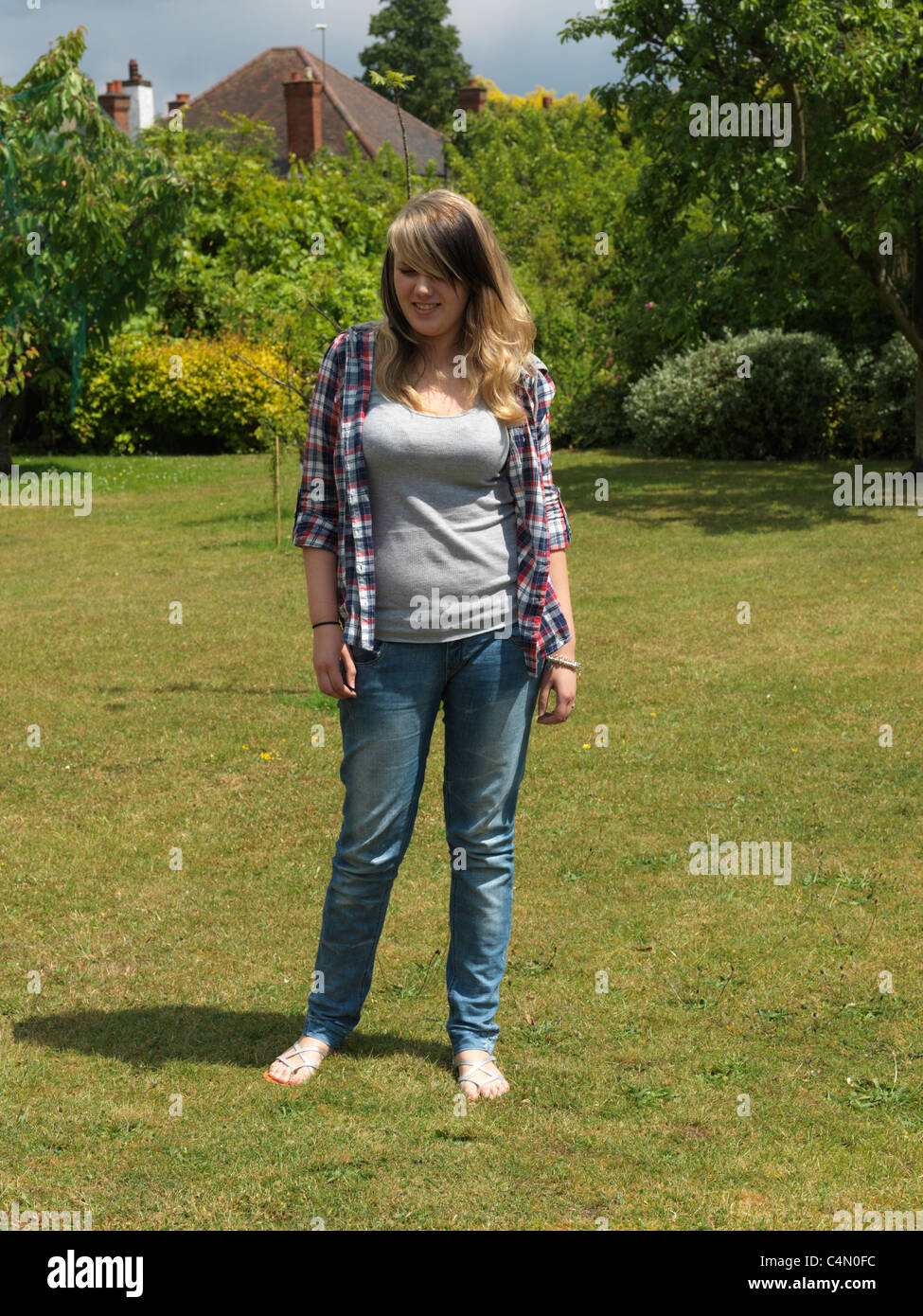 Young Woman Out In The Garden Wearing Shirt, Jeans And Sandals Stock Photo