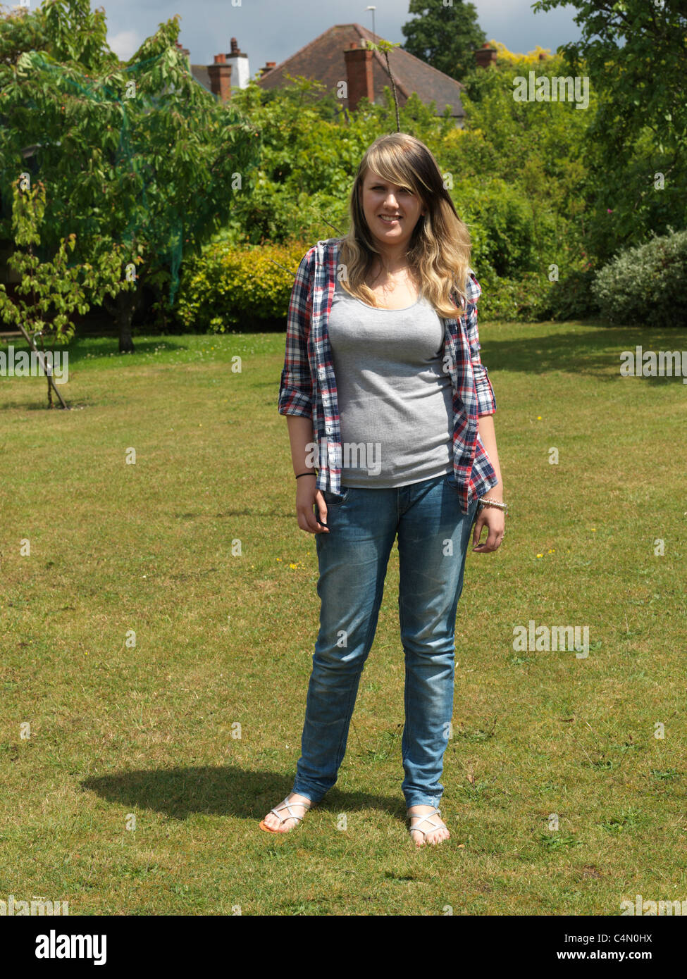Young Woman Out In The Garden Wearing Shirt, Jeans And Sandals Stock Photo