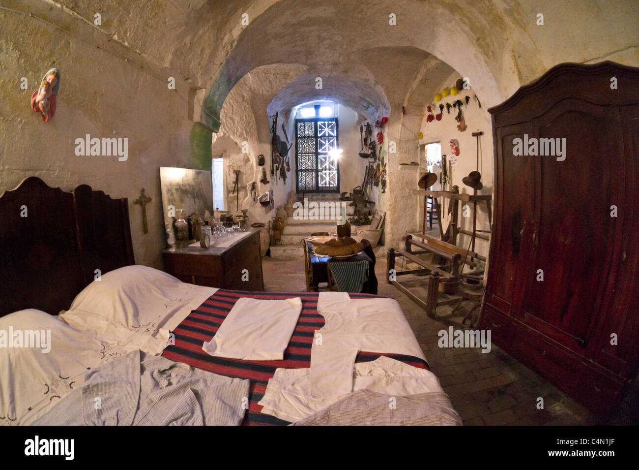 Italy - historic cave house in the Sassi Caveoso of Matera. Casa Grotta di Casalnuevo. High bed, linen, wardrobe and loom. Stock Photo