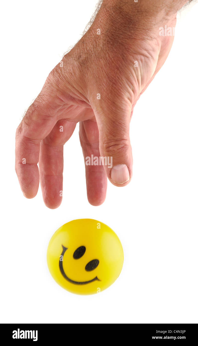 Mans hand grabbing  a yellow smiley rubber ball. Stock Photo