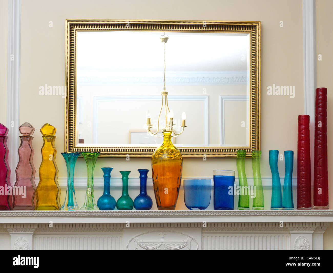 A Collection Different Coloured And Shapes Bottles And Vases Made From Recycled Glass In A Row On A Mantlepiece By A Mirror Stock Photo