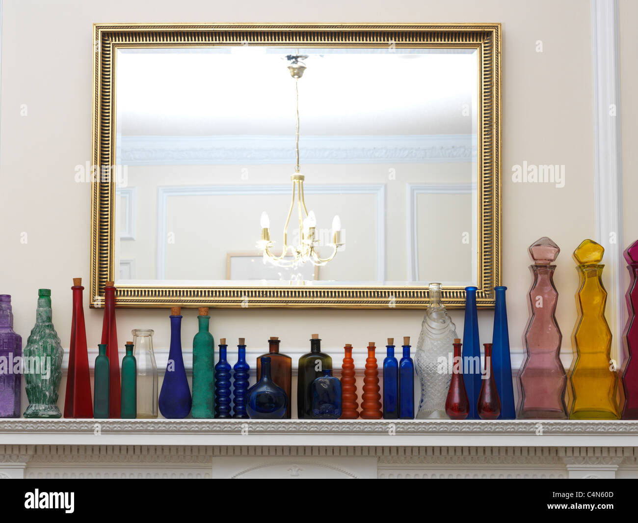 A Collection Of Glass Bottles All Different Shapes, Sizes And Colours In A Row On A Mantlepiece Stock Photo