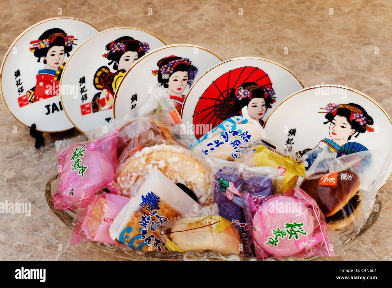 A set of miniature decorative Japanese plates on display behind an assortment of individually wrapped Japanese cookies. Stock Photo
