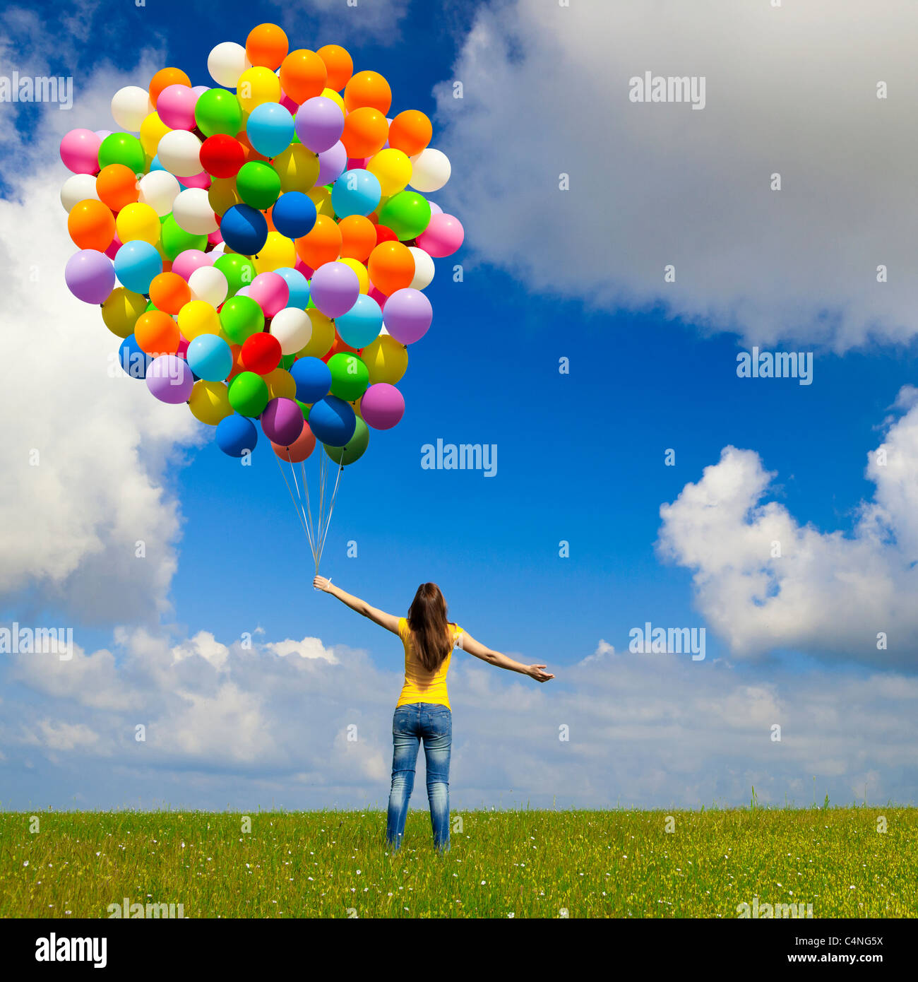 Happy young woman with colorful balloons on a green meadow Stock Photo