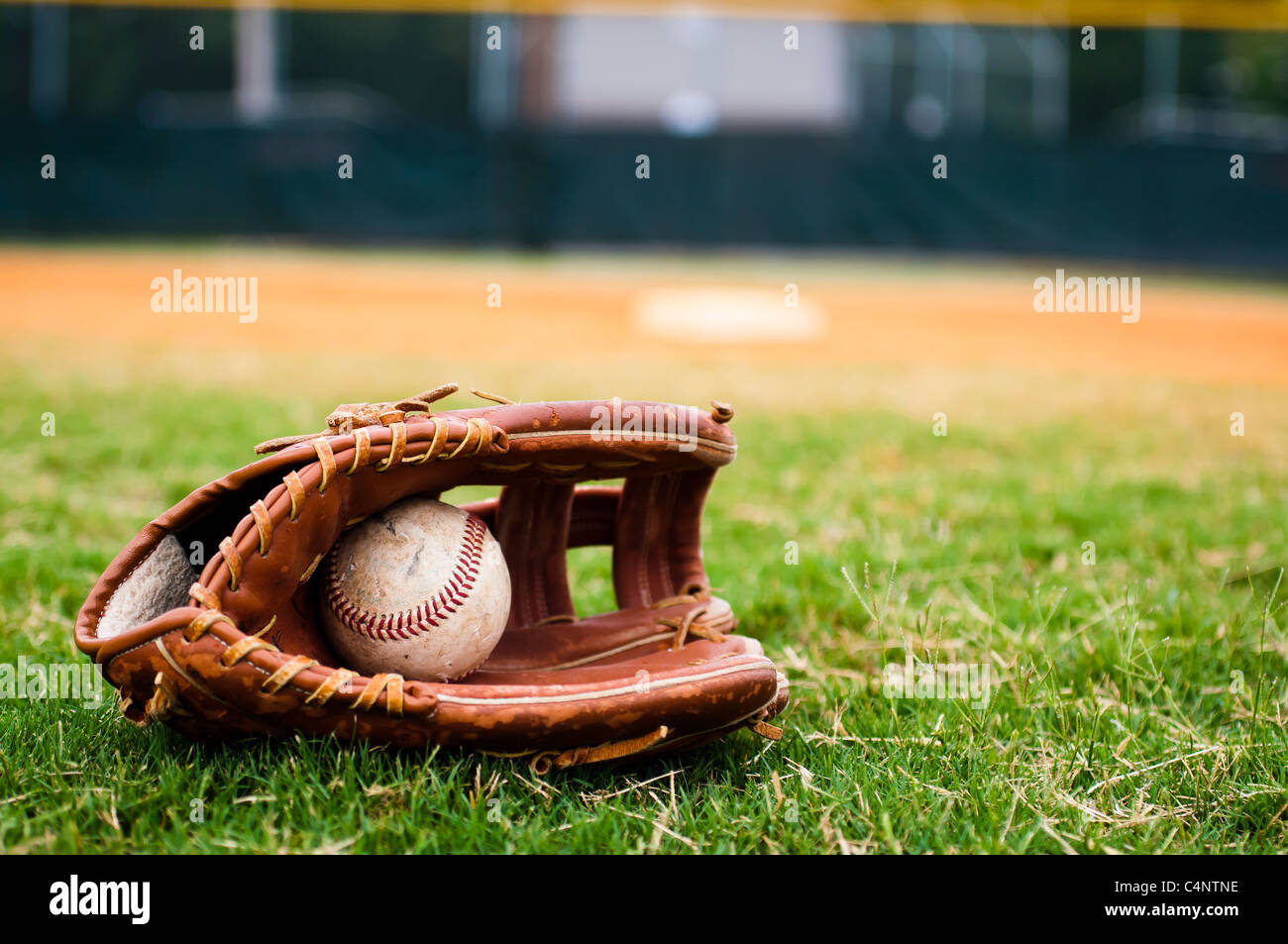 Baseball in glove on field with base and outfield in background. Stock Photo