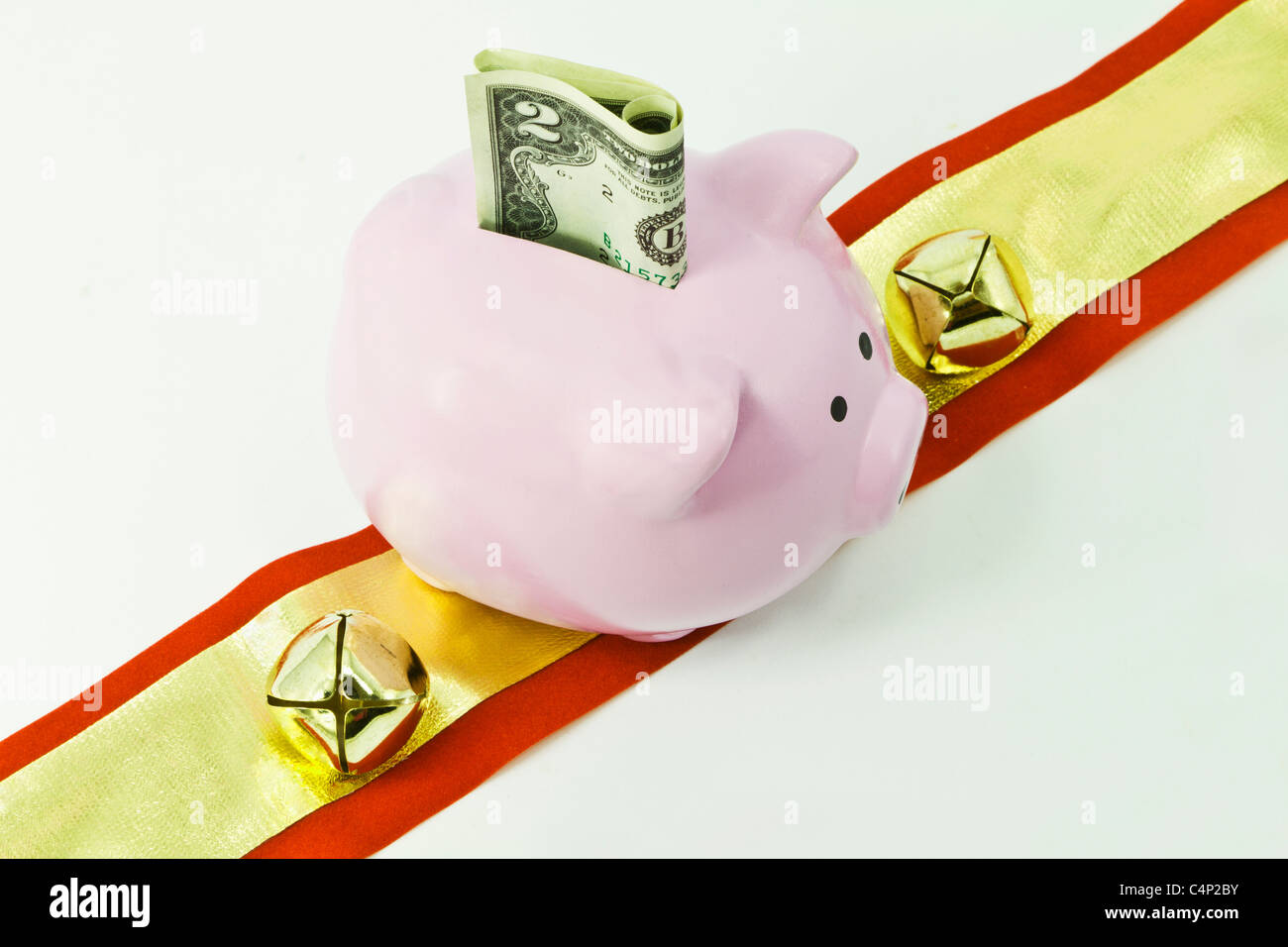 Pink pig-shaped bank with USA currency, red and gold ribbon, and gold bells. Stock Photo