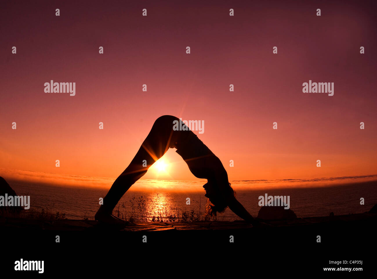 21-year-old woman in downward dog yoga position by seashore at sunset Stock Photo