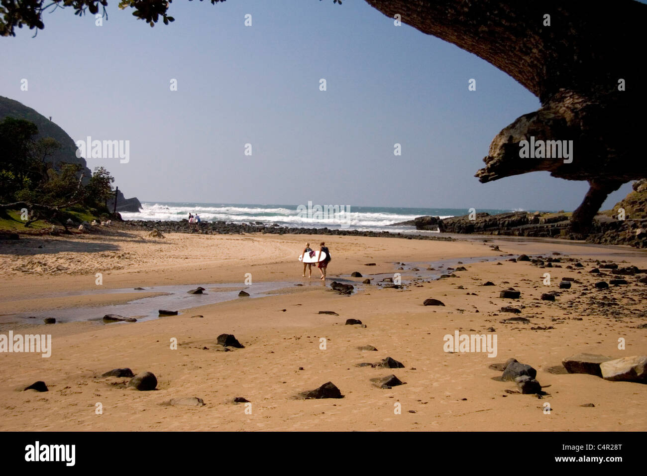 Surfers walking along beach towards the ocean, Coffee Bay, Transkei, South Africa Stock Photo