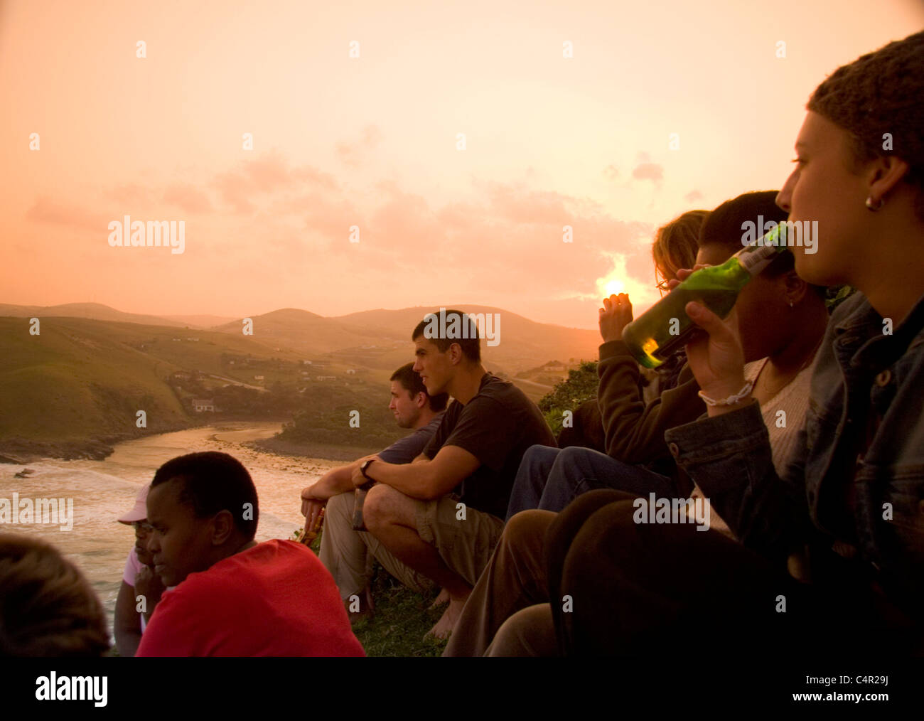 A group of tourists sit hillside overlooking Coffee Bay enjoying the sunset, Transkei, South Africa Stock Photo