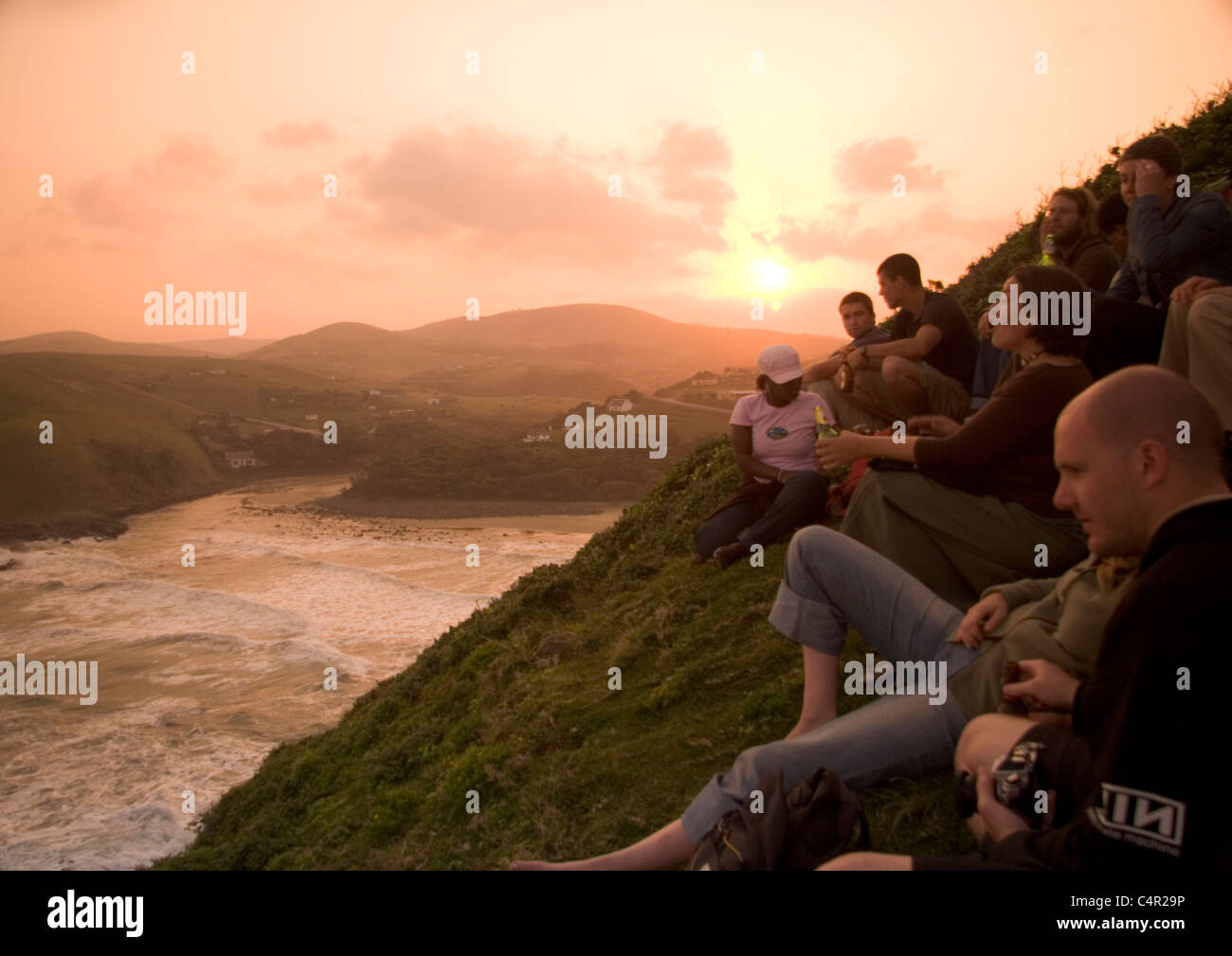 A group of tourists sit hillside overlooking Coffee Bay enjoying the sunset, Transkei, South Africa Stock Photo