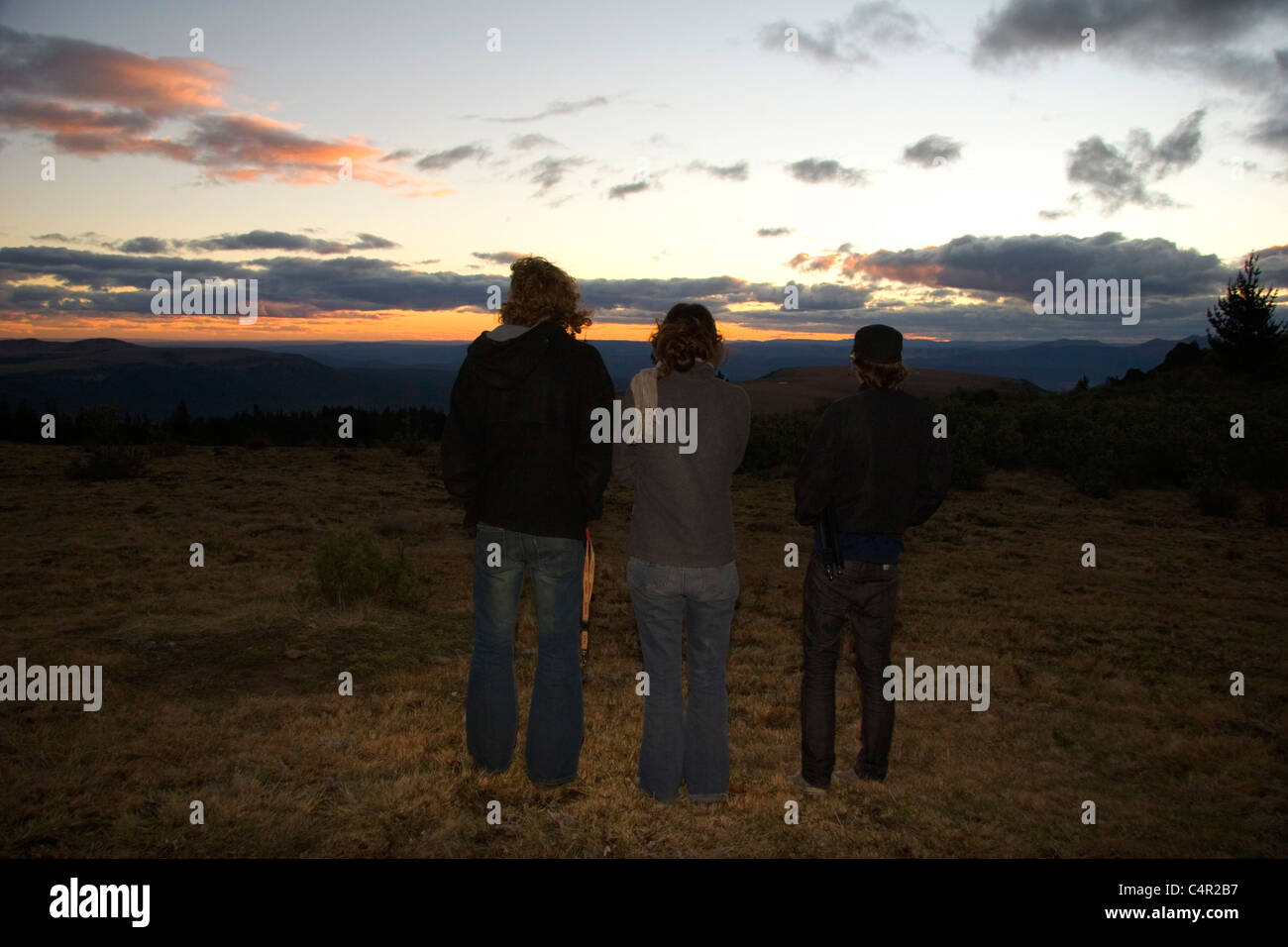 Three people viewing sunset in field by Hogsback Mountain, Amatola Mountains of South Africa Stock Photo