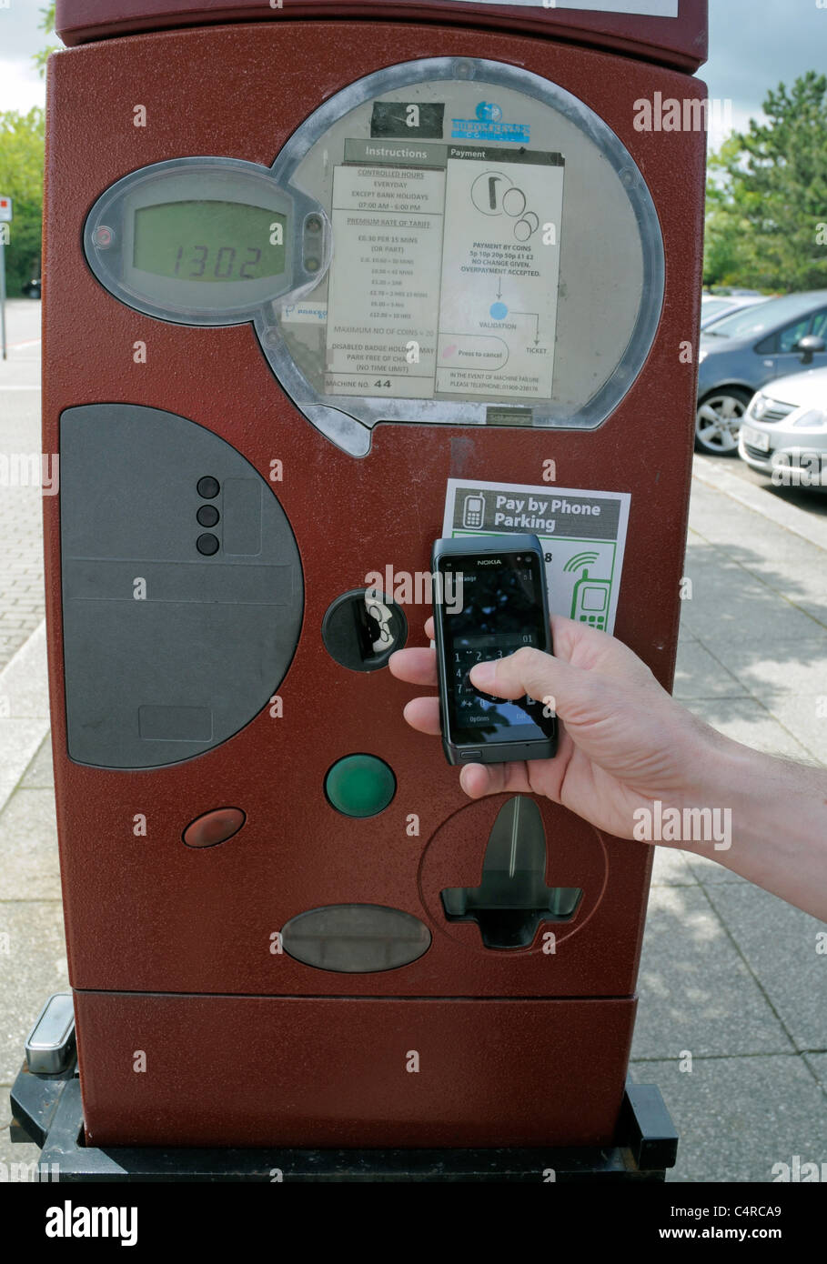 A Pay by Mobile Phone Parking Meter with Man holding Mobile Phone in Hand ready to Pay Charges Stock Photo