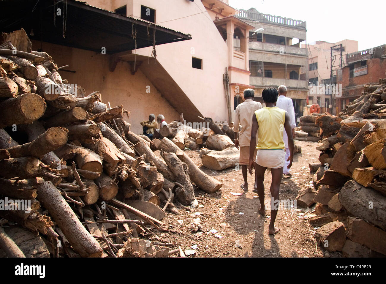 Locals walking by pile of wood used for the burning ghats, Varanasi, India Stock Photo