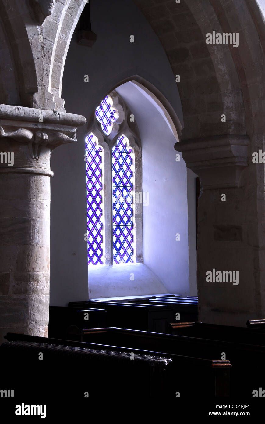 An arched stained glass window in a church with pillar and pews UK