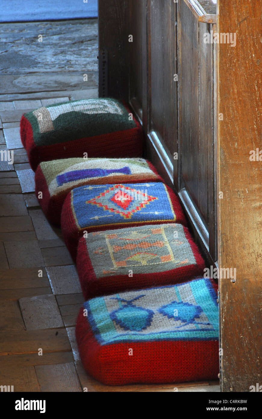 A variety of colourful hassocks in front of a pew in a church UK Stock Photo