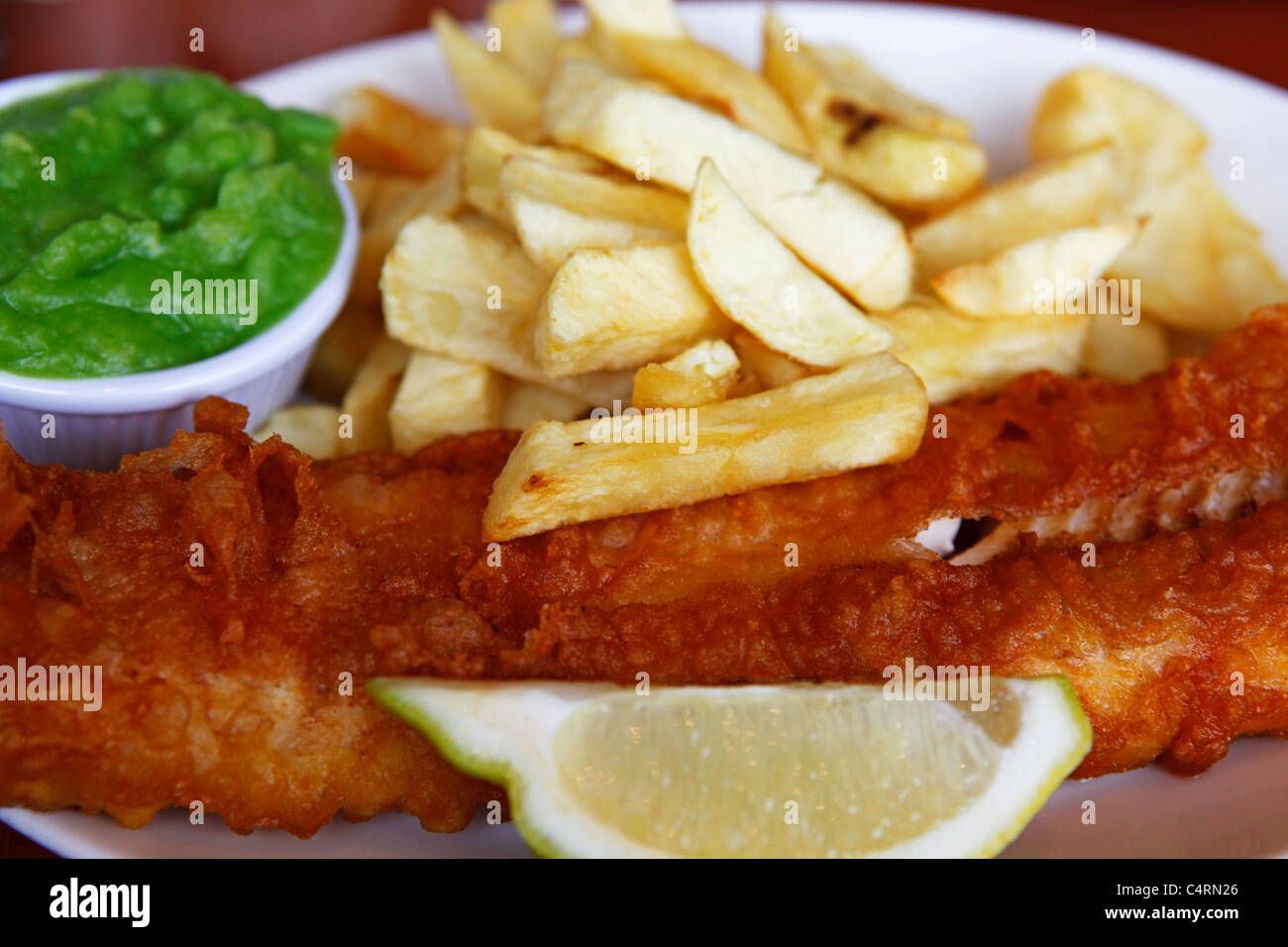 Close up of a plate of fish and chips, served with mushy peas and a wedge of lemon. Stock Photo