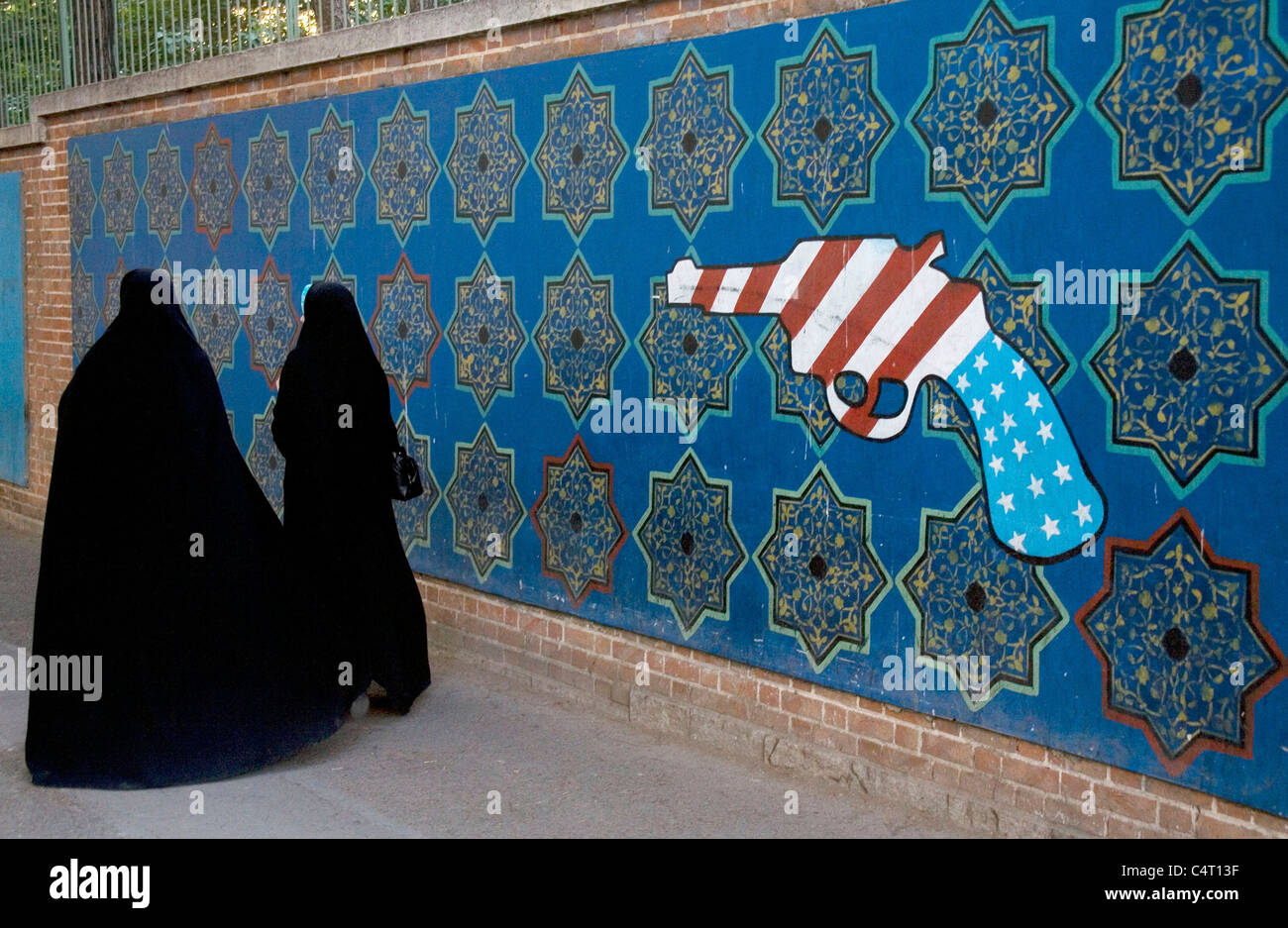 Iranian women walking on the sidewalk in Tehran, Iran with American gun on wall Stock Photo