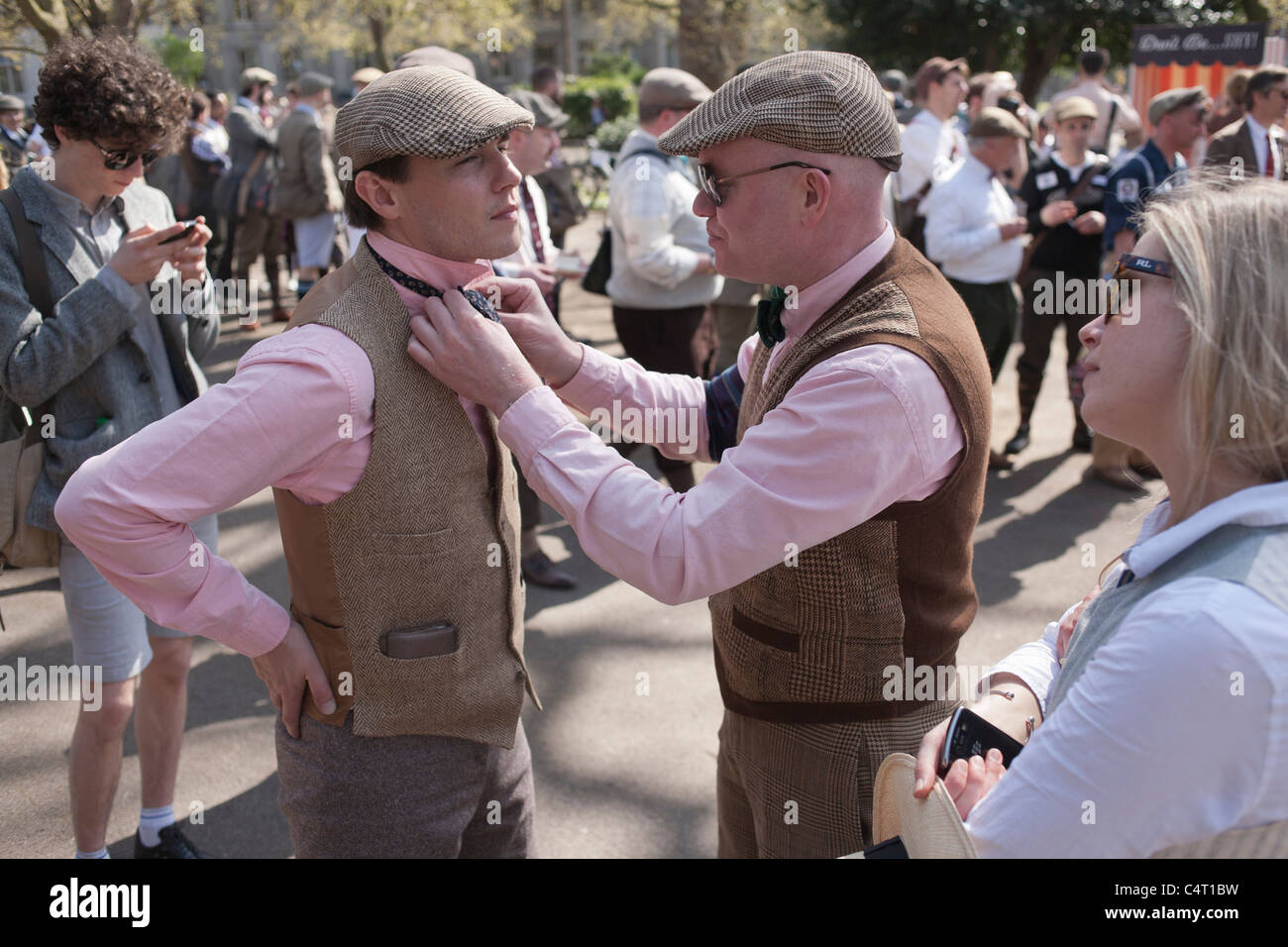 A man in a tweed vest fixes the bow tie on his matching friend at the London Tweed Run, 2011 Stock Photo