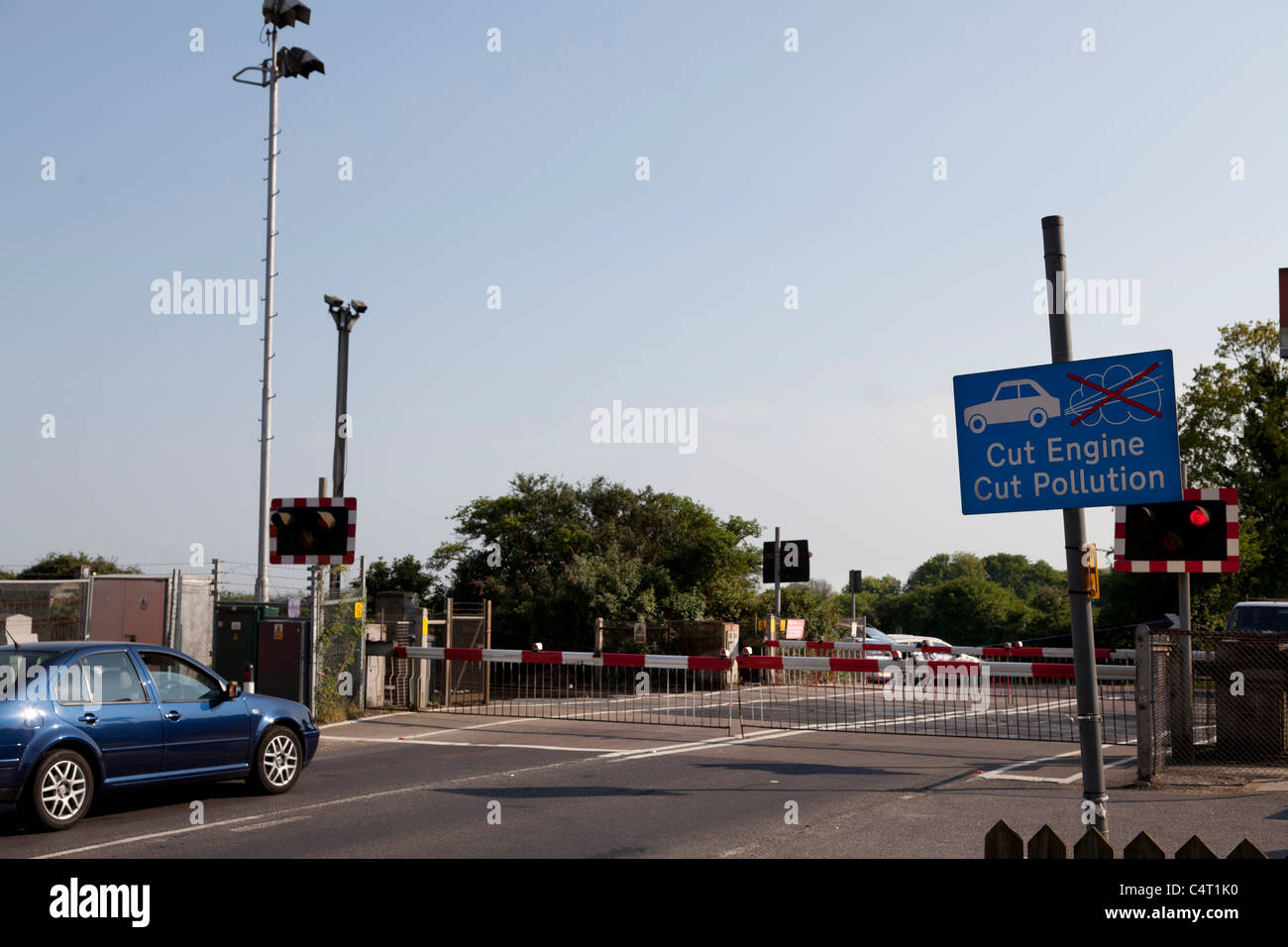 cars waiting at closed railway level crossing with cut engine cut pollution sign Stock Photo