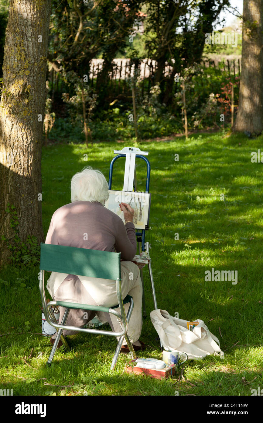 artist on stool painting under some trees on a sunny day Stock Photo