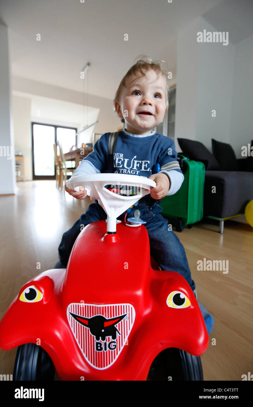 Little boy, 1 year old, is exploring his home. curiously exploring the apartment. On a toy car, Bobby car. Stock Photo