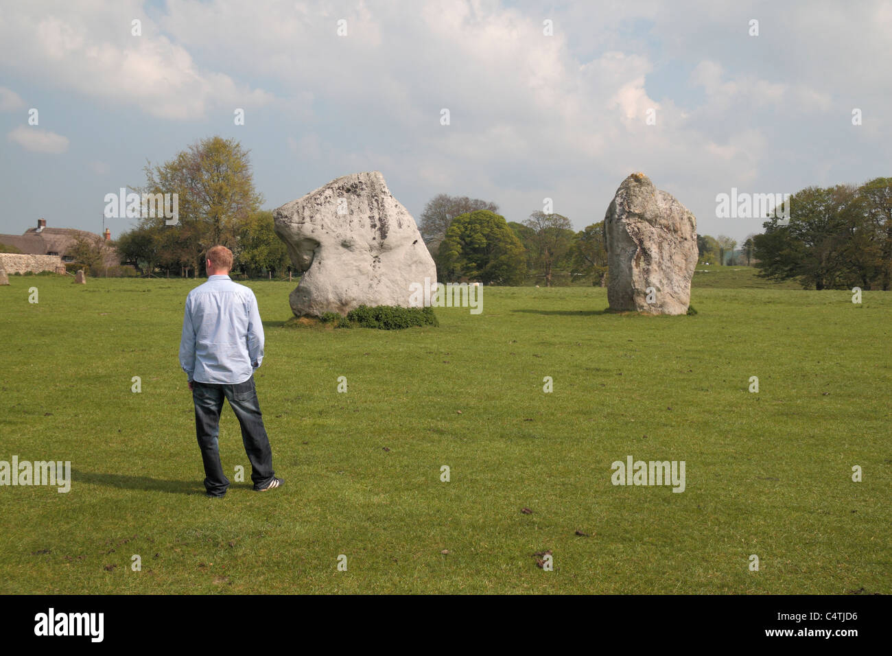 A visitor standing in front of several sarsen stones, part of the Avebury Henge & Stone Circles site, Wiltshire, England. Stock Photo