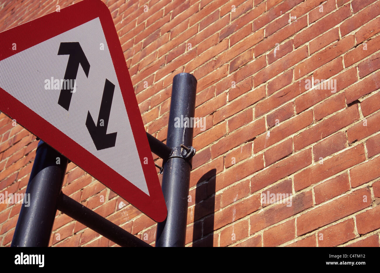 Red white and black triangular roadsign with opposing arrows showing Two-way traffic mounted on bracket next to brickwall Stock Photo