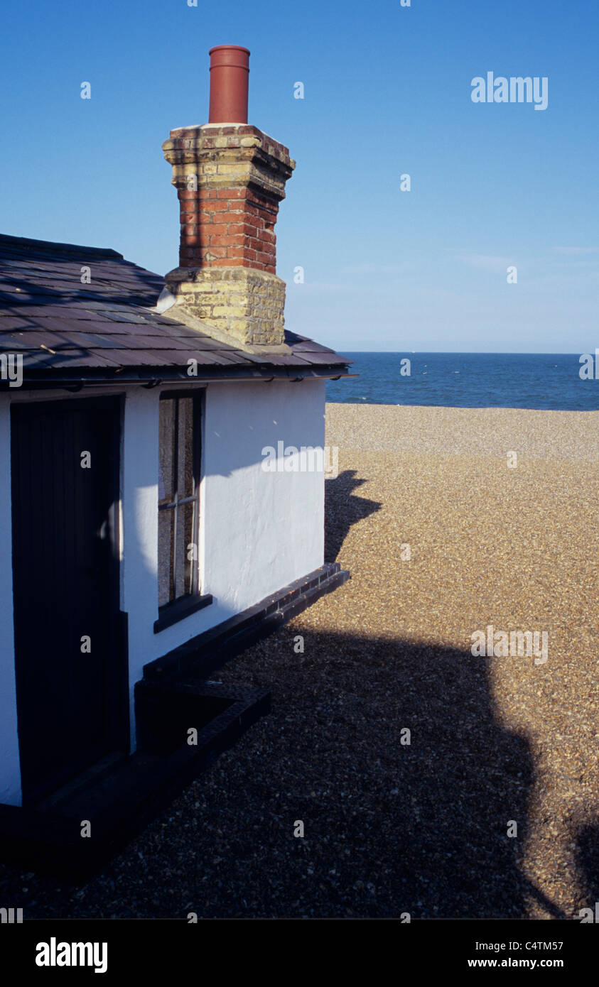 Detail of single-storey house or lodge with disproportionately large brick chimney on shingle beach with shadows and blue sea Stock Photo