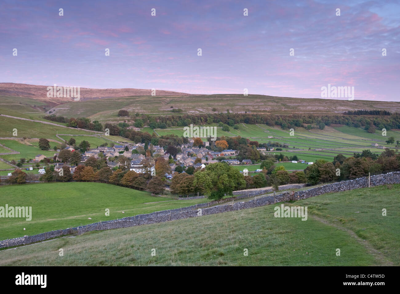 Kettlewell village, nestling in scenic rural valley below upland hills & moors & pink evening sunset sky - Wharfedale, Yorkshire Dales, England, UK. Stock Photo