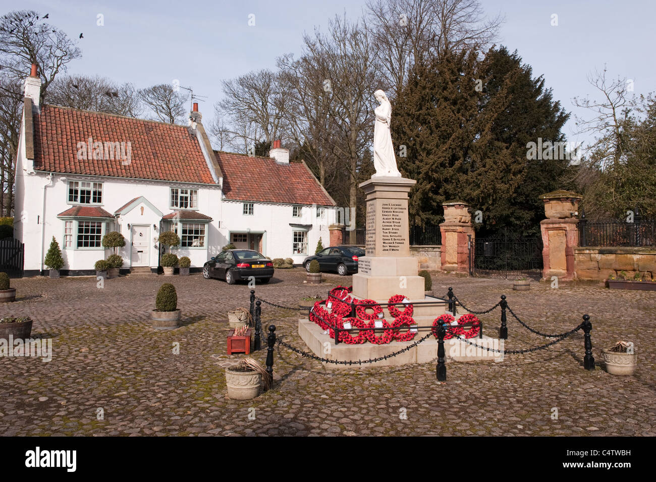 Red poppy wreaths laid at base of WW1 & WW2 war memorial in attractive rural town - cobbled Hall Square, Boroughbridge, North Yorkshire, England, UK. Stock Photo