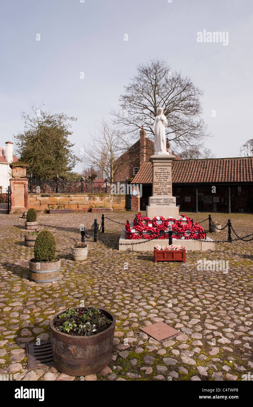 Red poppy wreaths laid at base of WW1 & WW2 war memorial in attractive rural town - cobbled Hall Square, Boroughbridge, North Yorkshire, England, UK. Stock Photo