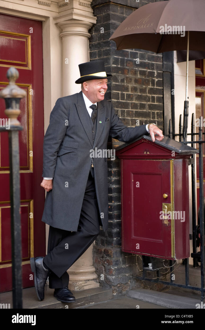 London Mayfair Curzon Street Aspinalls Gaming Club front door entrance laughing smiling doorman top hat & grey frock coat with raised umbrella Stock Photo