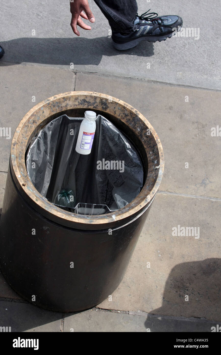 A plastic bottle being thrown into a waste bin with the hand and foot of the thrower at the top of the image Stock Photo