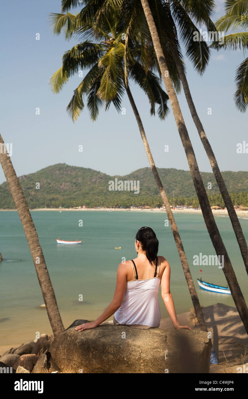 A young woman sits among palm trees high over the ocean at Palolem Beach, in Goa state, India Stock Photo