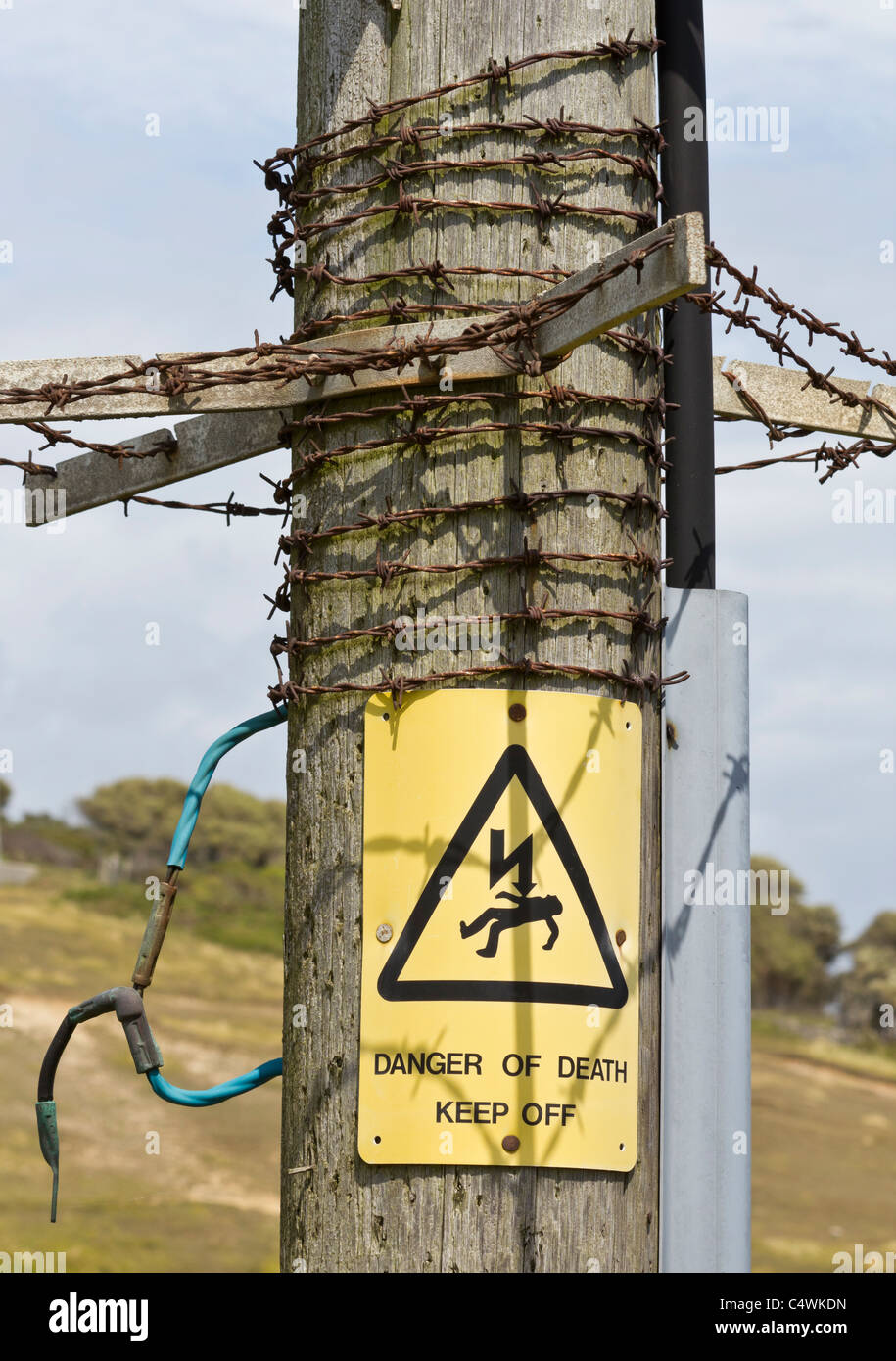 Danger of Death Keep Off sign on electricity pole pylon with barbed wire Stock Photo
