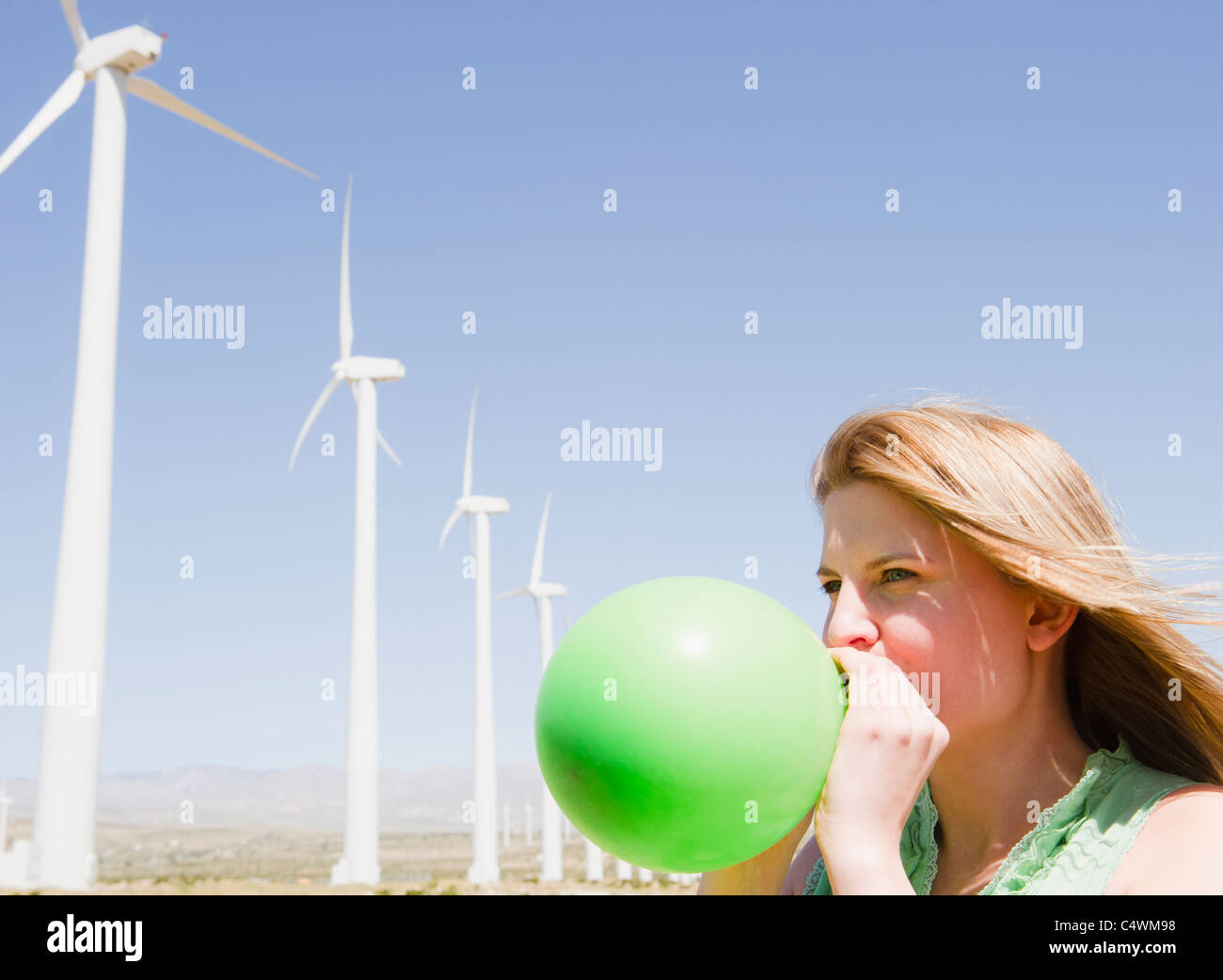 USA, California, Palm Springs, Coachella Valley, San Gorgonio Pass, Woman blowing green balloon with wind turbines in background Stock Photo