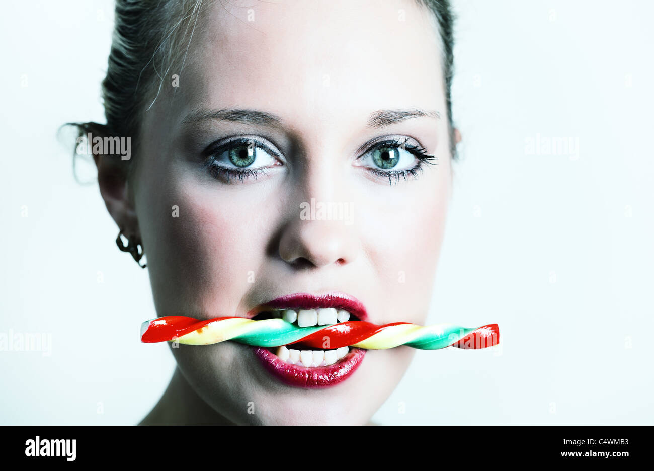 Portait of young woman holding colorful candy in her teeth Stock Photo