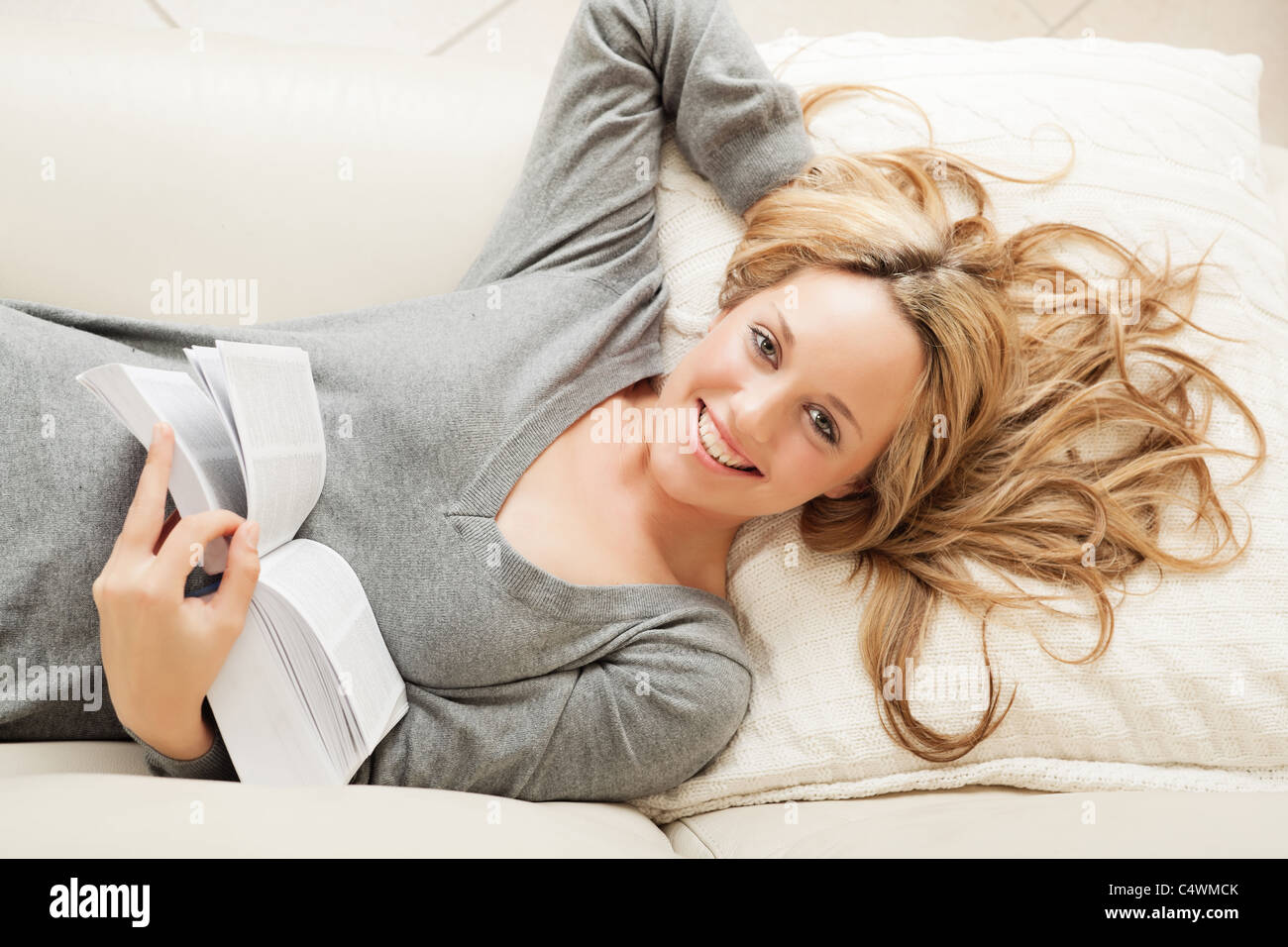 High angle view on smiling blond woman lying on sofa with book Stock Photo