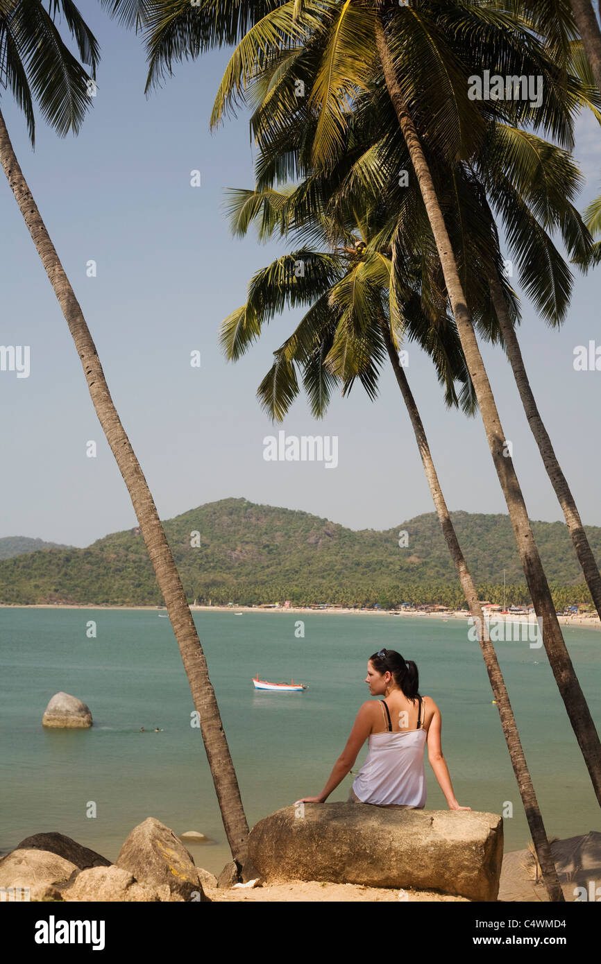 A young woman sits amidst palm trees high up over the ocean at Palolem Beach, in Goa state, India Stock Photo