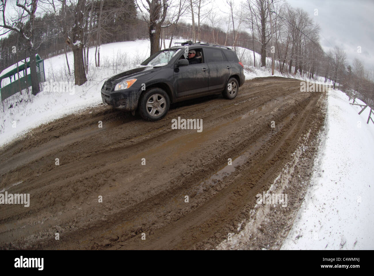 A car makes it’s way along a muddy road during mud season in Vermont in the spring. Stock Photo