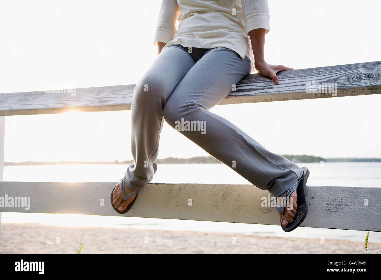 USA,New York State,Long Island,legs of woman sitting on rail fence,lake in background Stock Photo
