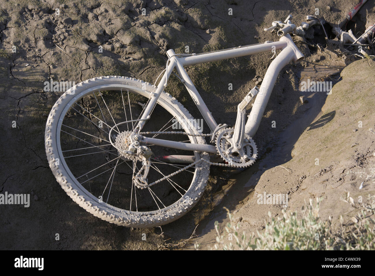 Broken bicycle lies abandoned and discarded in the mud of a river Stock
