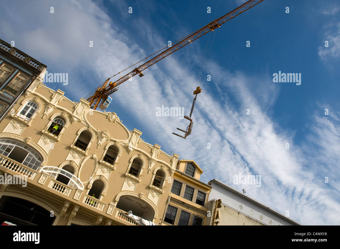 A builder fitting a window to a new building in Porto.  Little health and safety. Wide angle with crane. Stock Photo