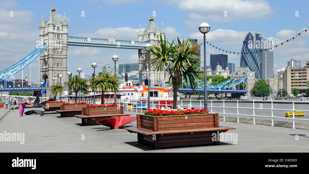 Thames Path at Butlers Wharf promenade views of River Thames Tower Bridge & London skyline red flowers row of planter boxes cordyline trees London UK Stock Photo
